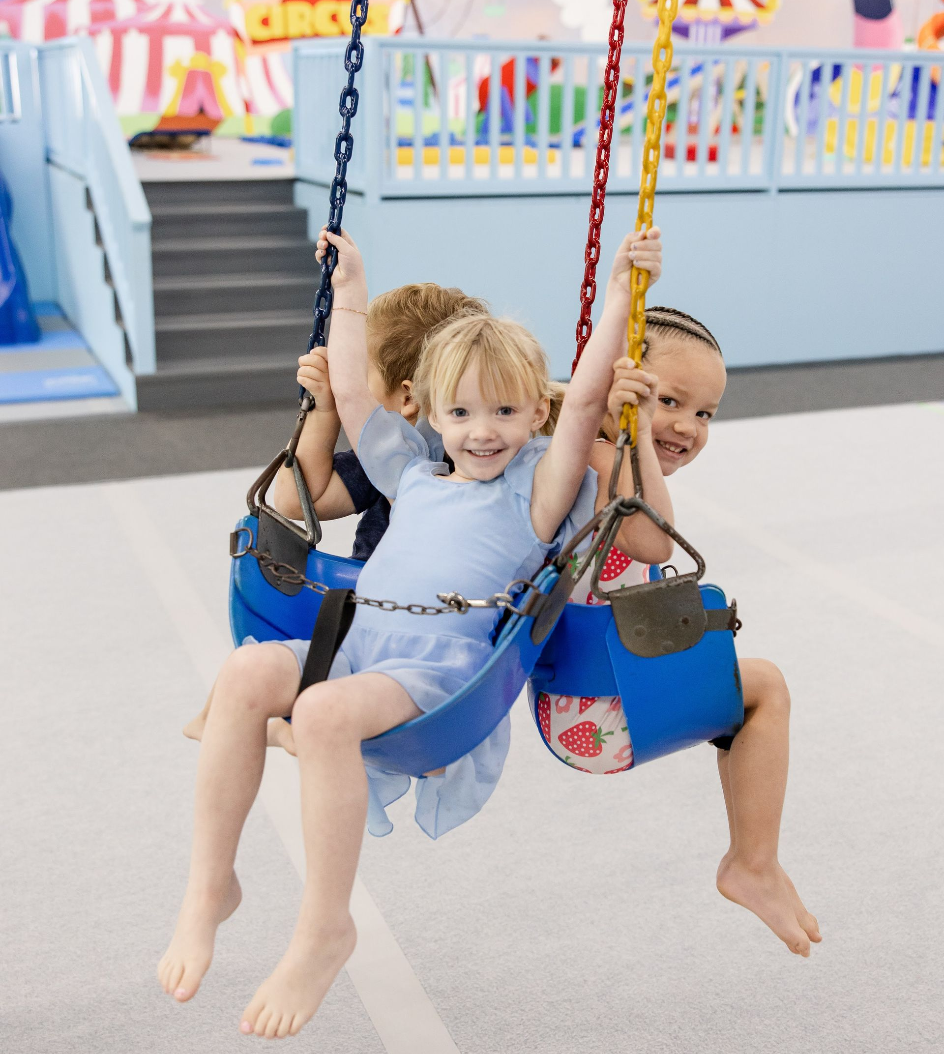 Two children sharing a swing, smiling in a colorful playground.