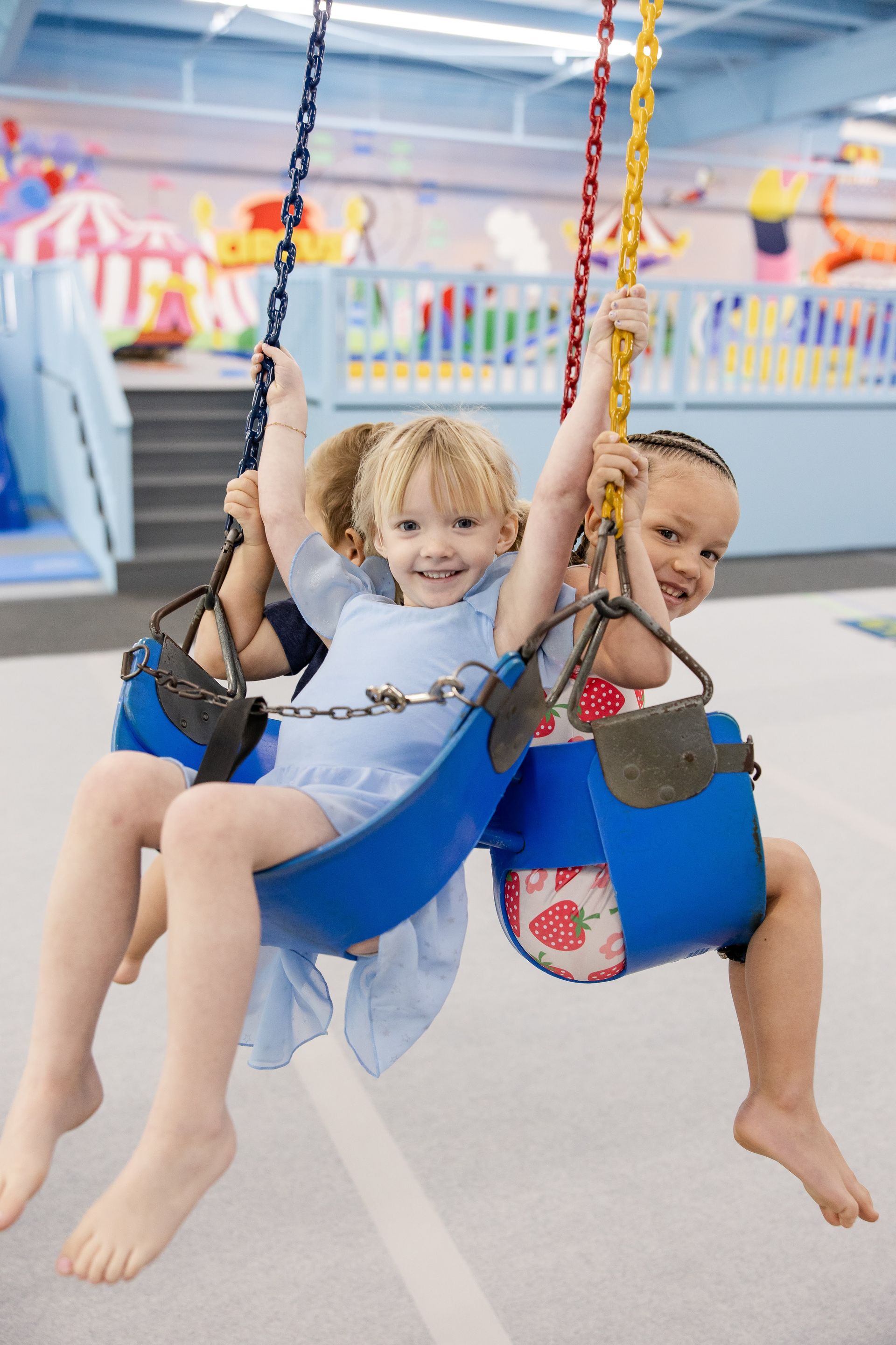 Thre children smiling on swings in a bright indoor play area