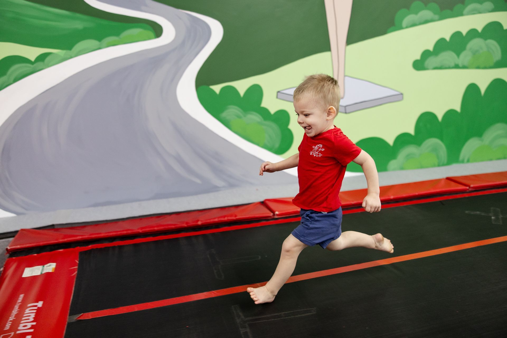 Child running on a trampoline beside a painted road mural