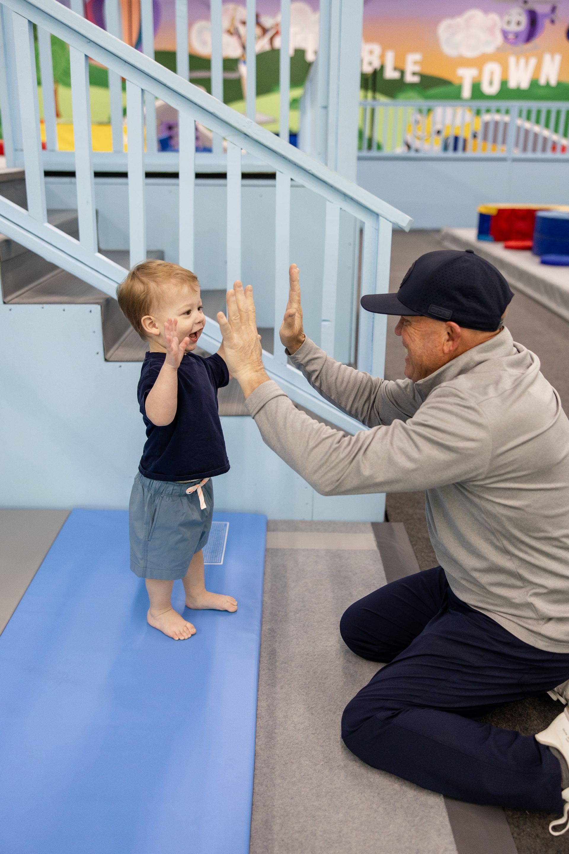 Adult kneeling with child for a high-five in a bright play area