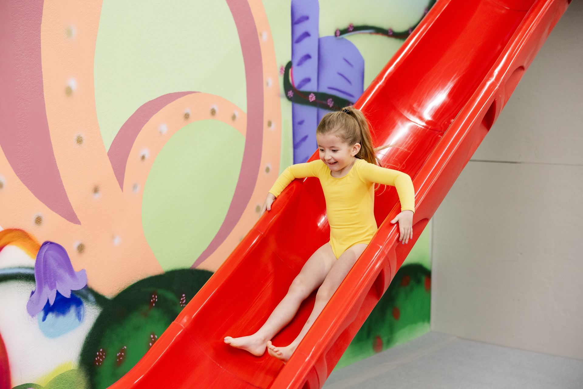Child sliding down a bright red slide in an indoor play area