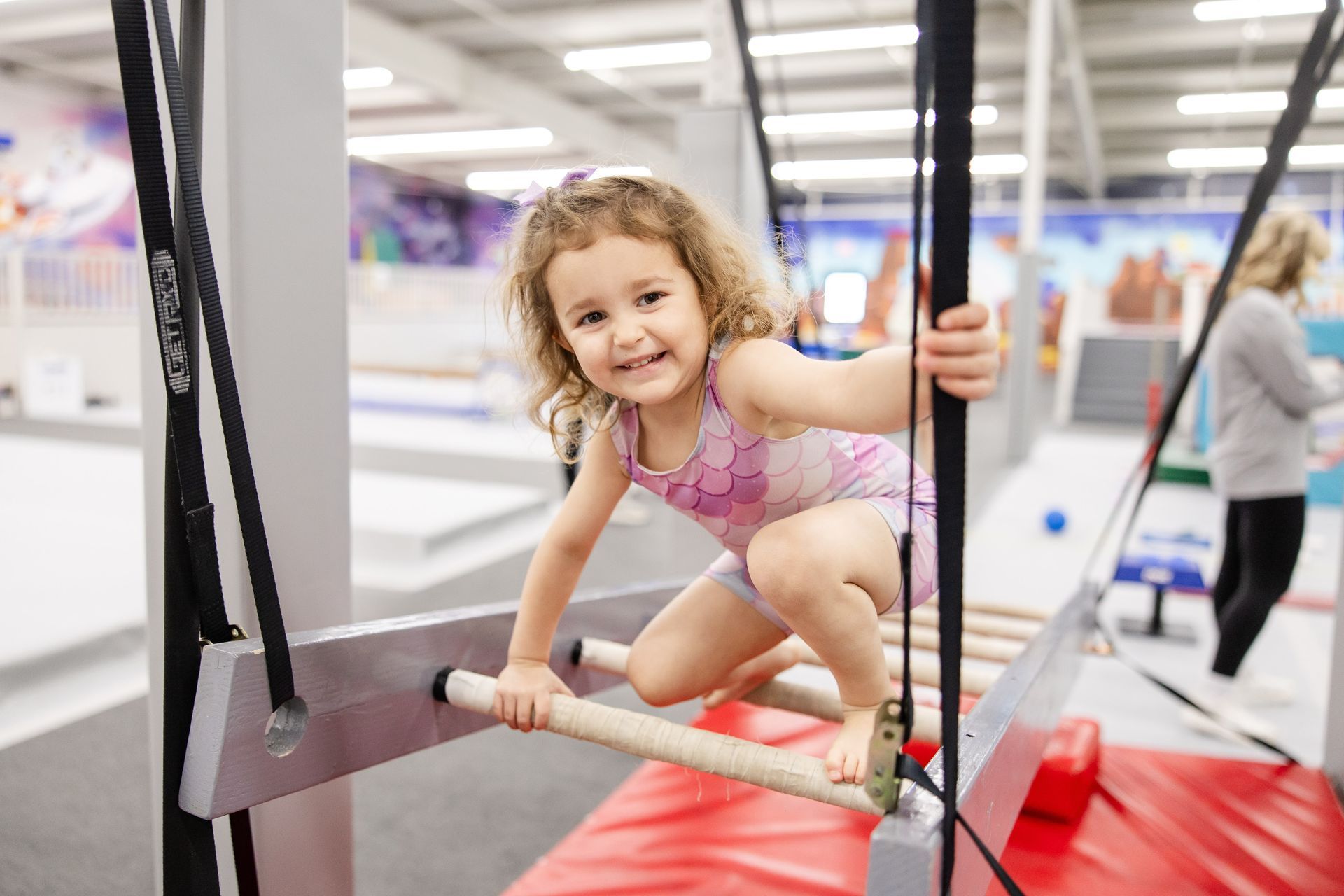 Child balancing on a trampoline beam, smiling in a gym play area