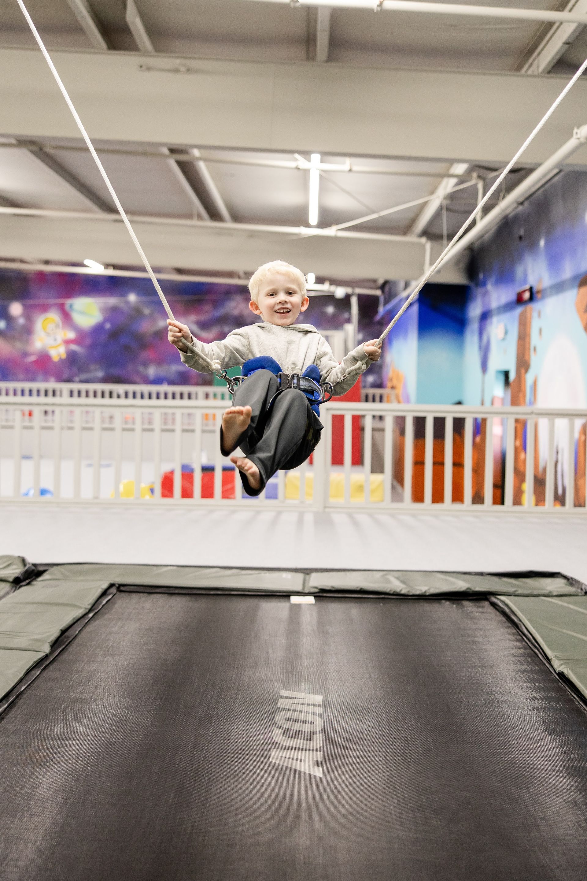 Child bouncing indoors on a trampoline, smiling in a colorful play area