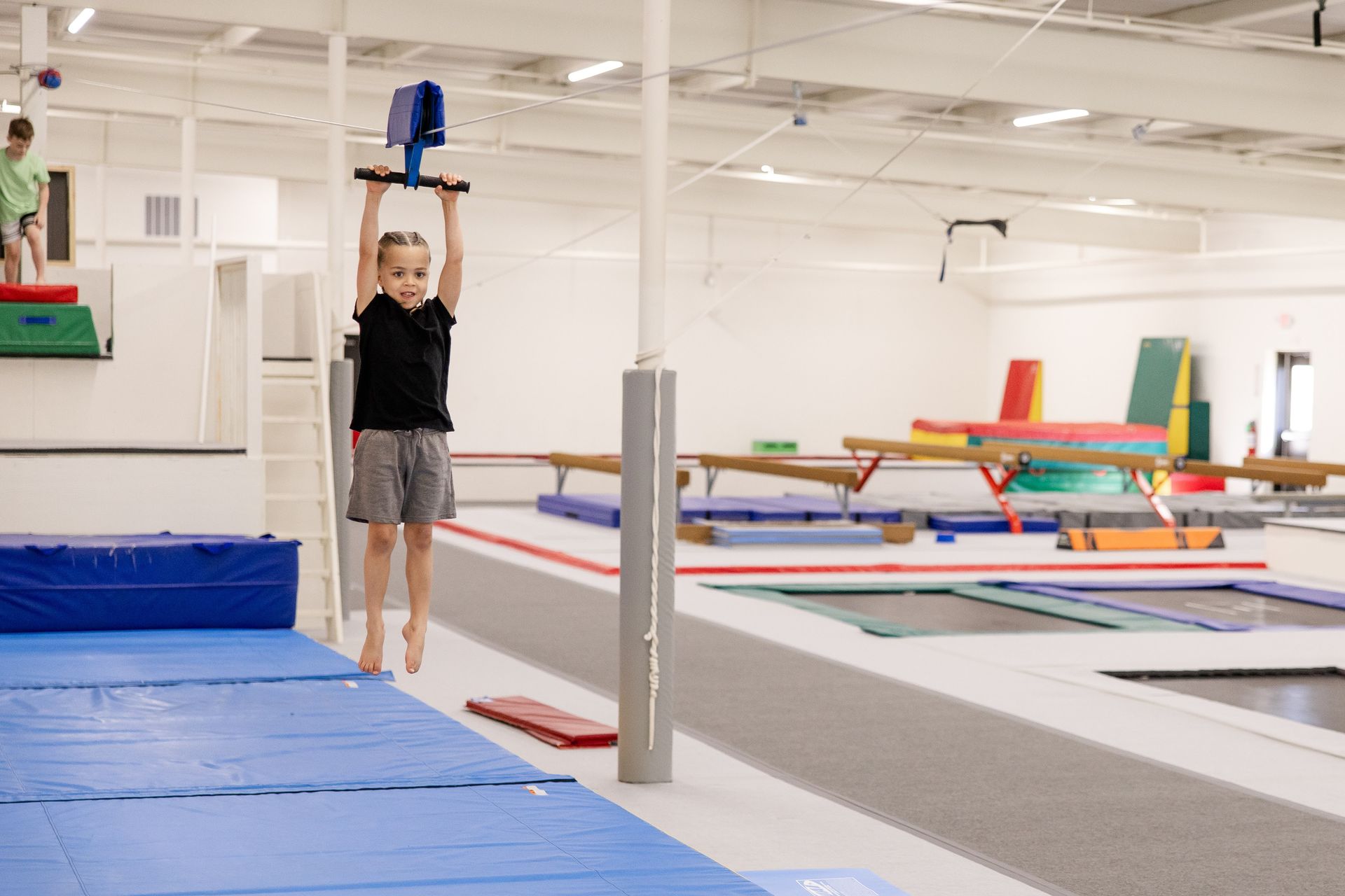 Person holding a blue object above their head in a gym with mats and trampolines