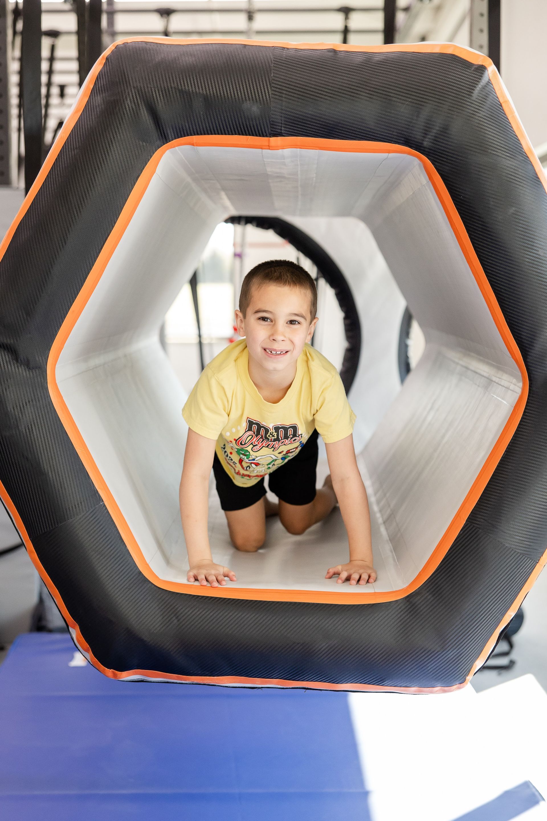 Child crawling through a black-and-orange hexagonal play tunnel indoors