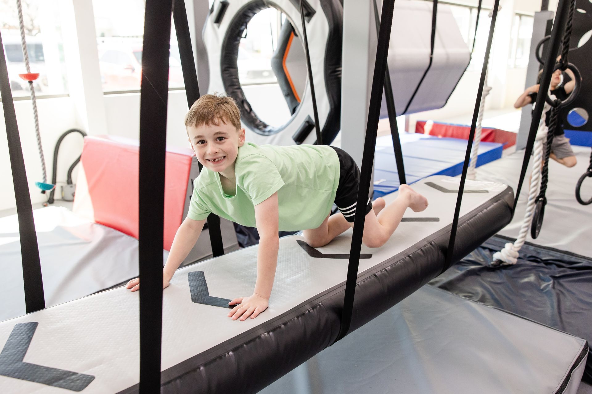 Child crawling on a foam obstacle in an indoor gym, with a playful smile.