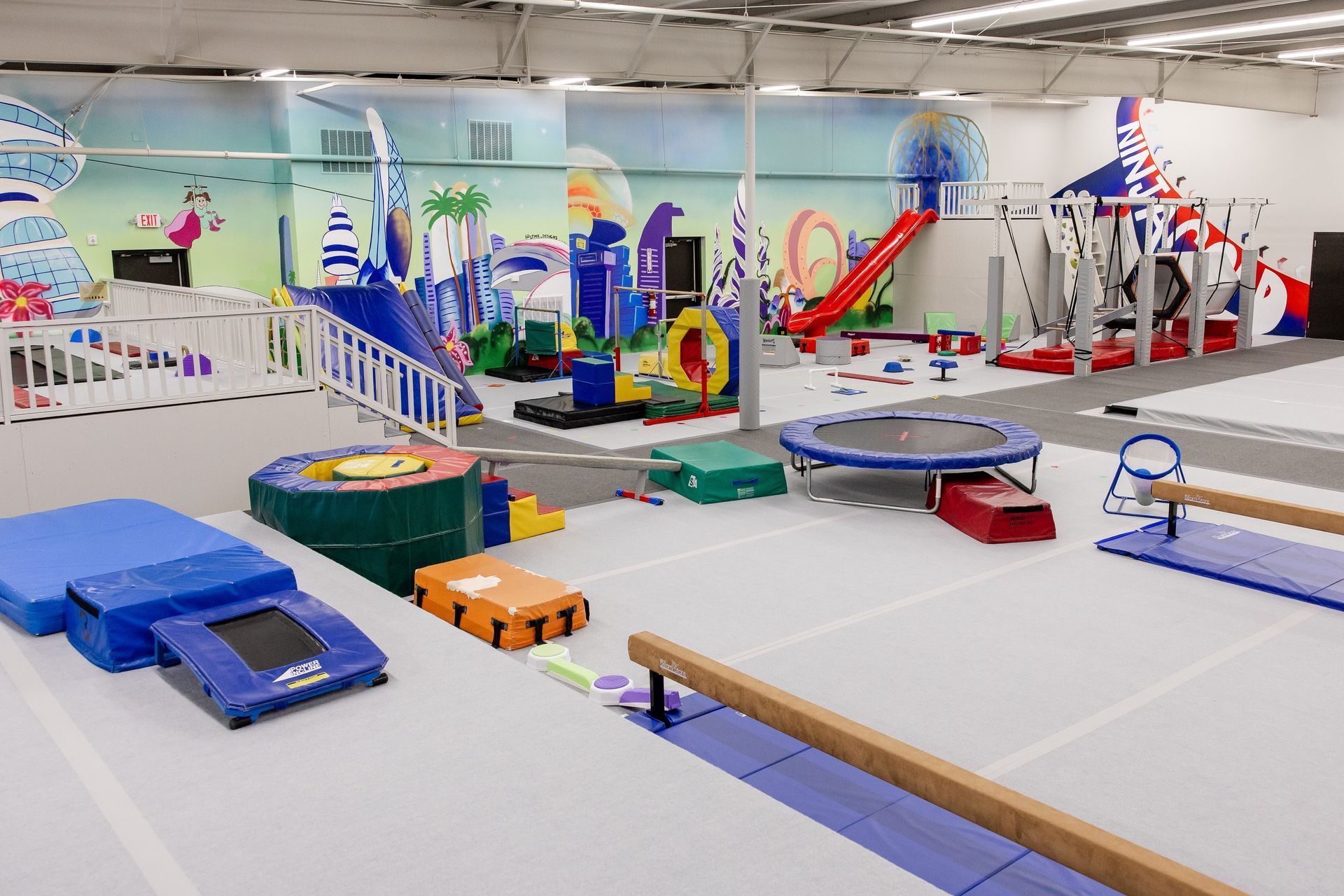 Gymnastics training room with foam pits, trampolines, balance beams, and colorful equipment.