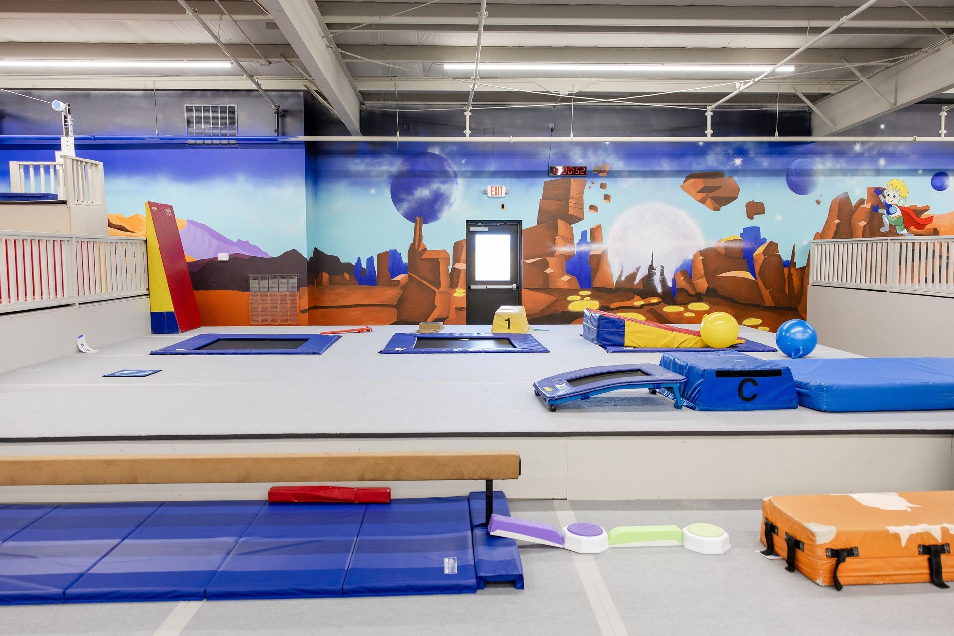 Indoor obstacle course with blue and orange padded equipment in a gymnasium, set before a desert mural.