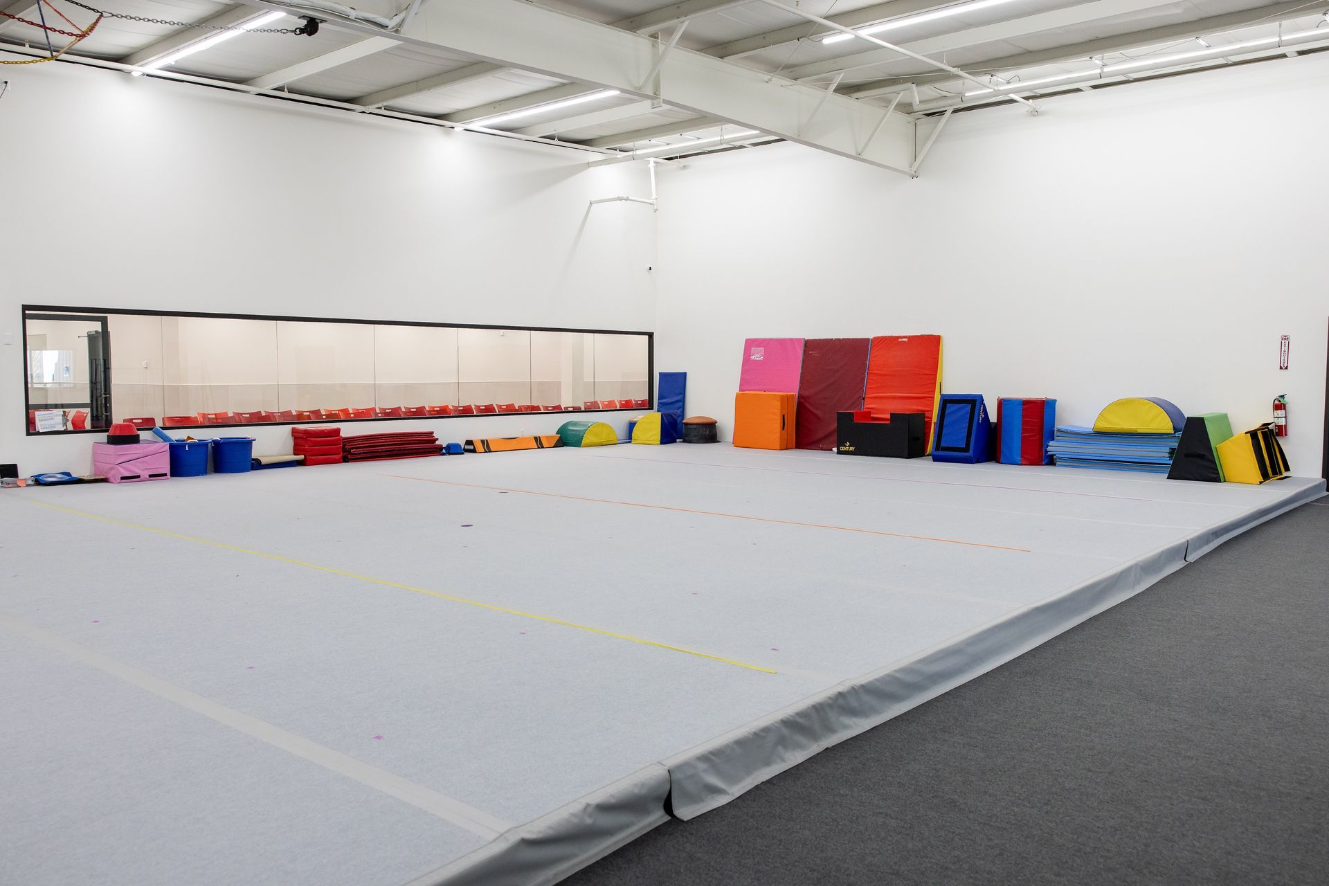 Empty gymnastics training area with mats, foam blocks, and safety pads in a large white gym