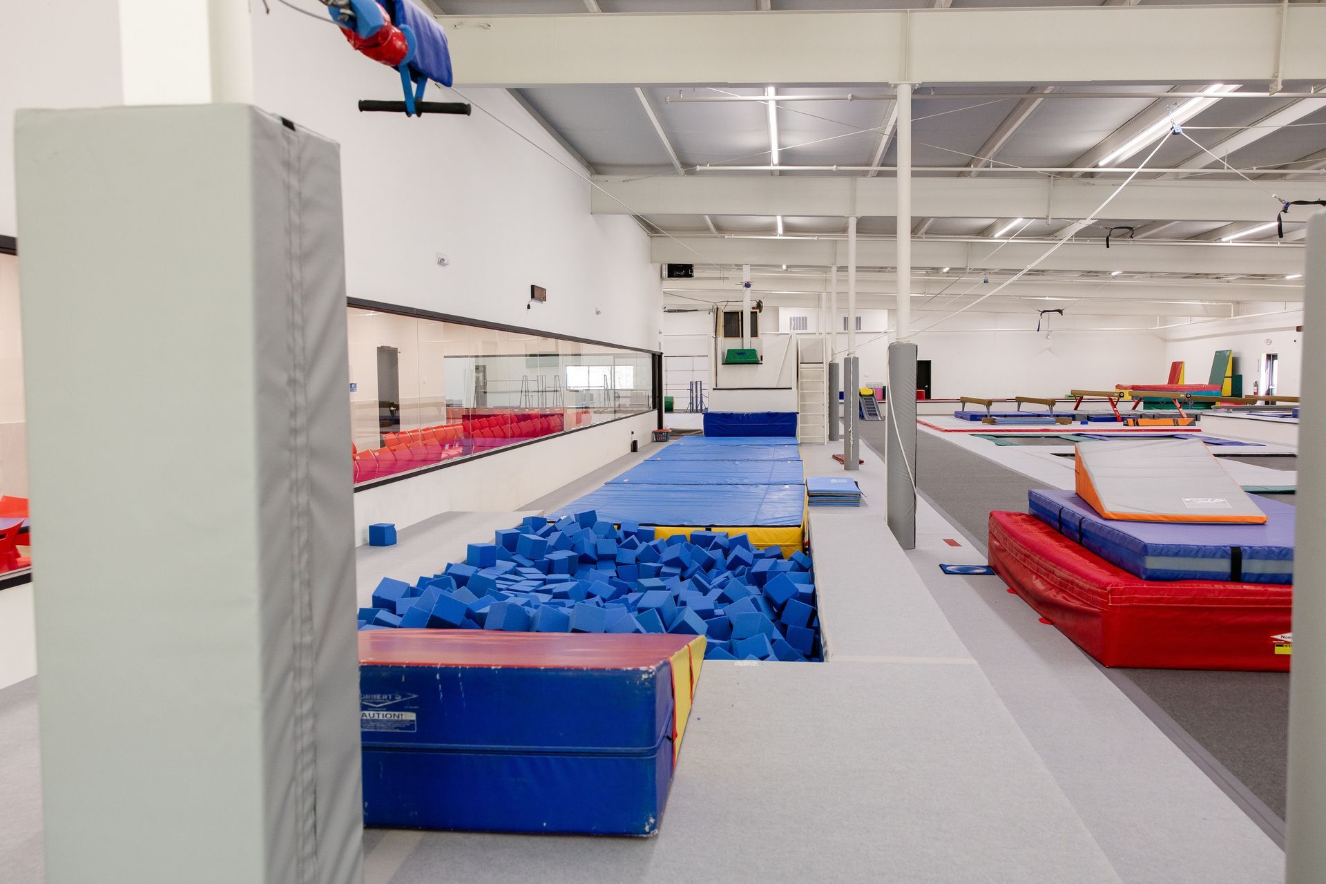 Indoor gym with blue foam pit, zipline, and trampolines in a bright open space