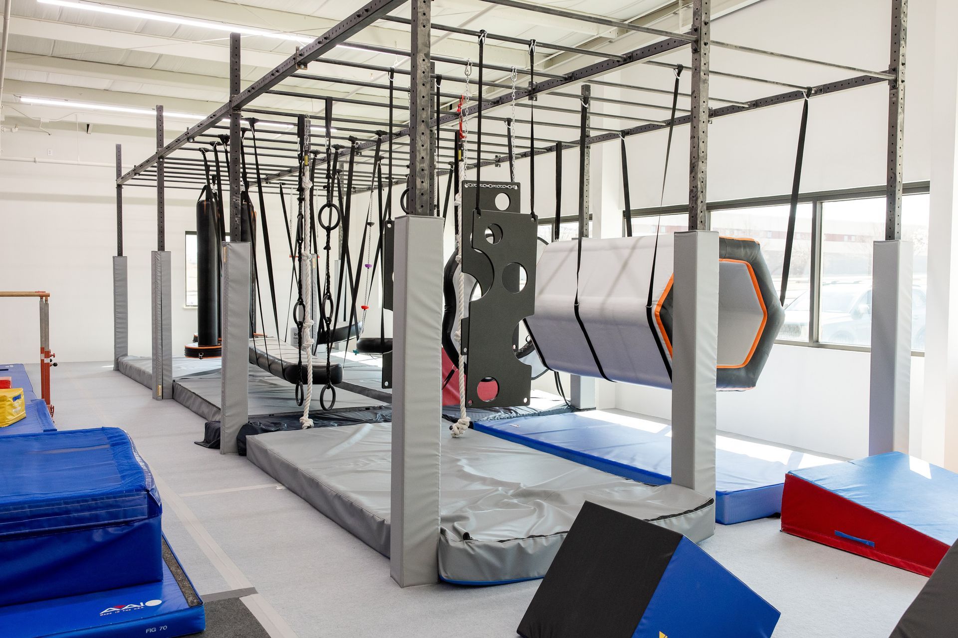 Indoor ninja training area with suspension frames, mats, and foam obstacles in a bright gym