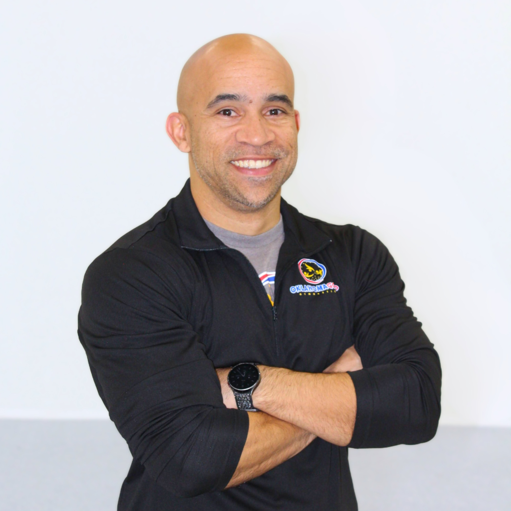 Smiling man in a black shirt with arms crossed against a light background