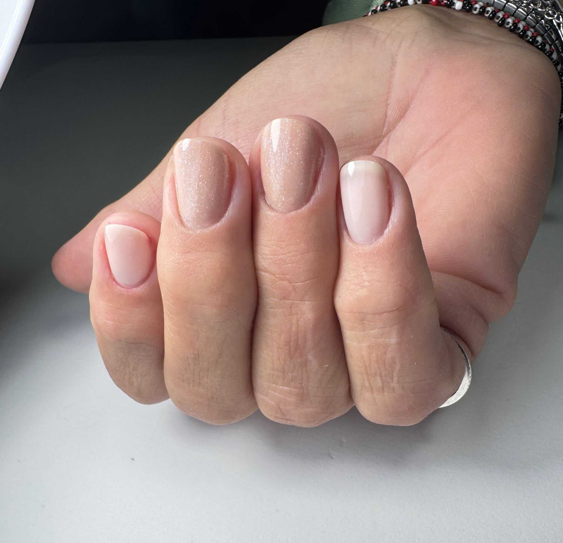 Hand met korte nagels, gelakt in lichte, neutrale tinten.