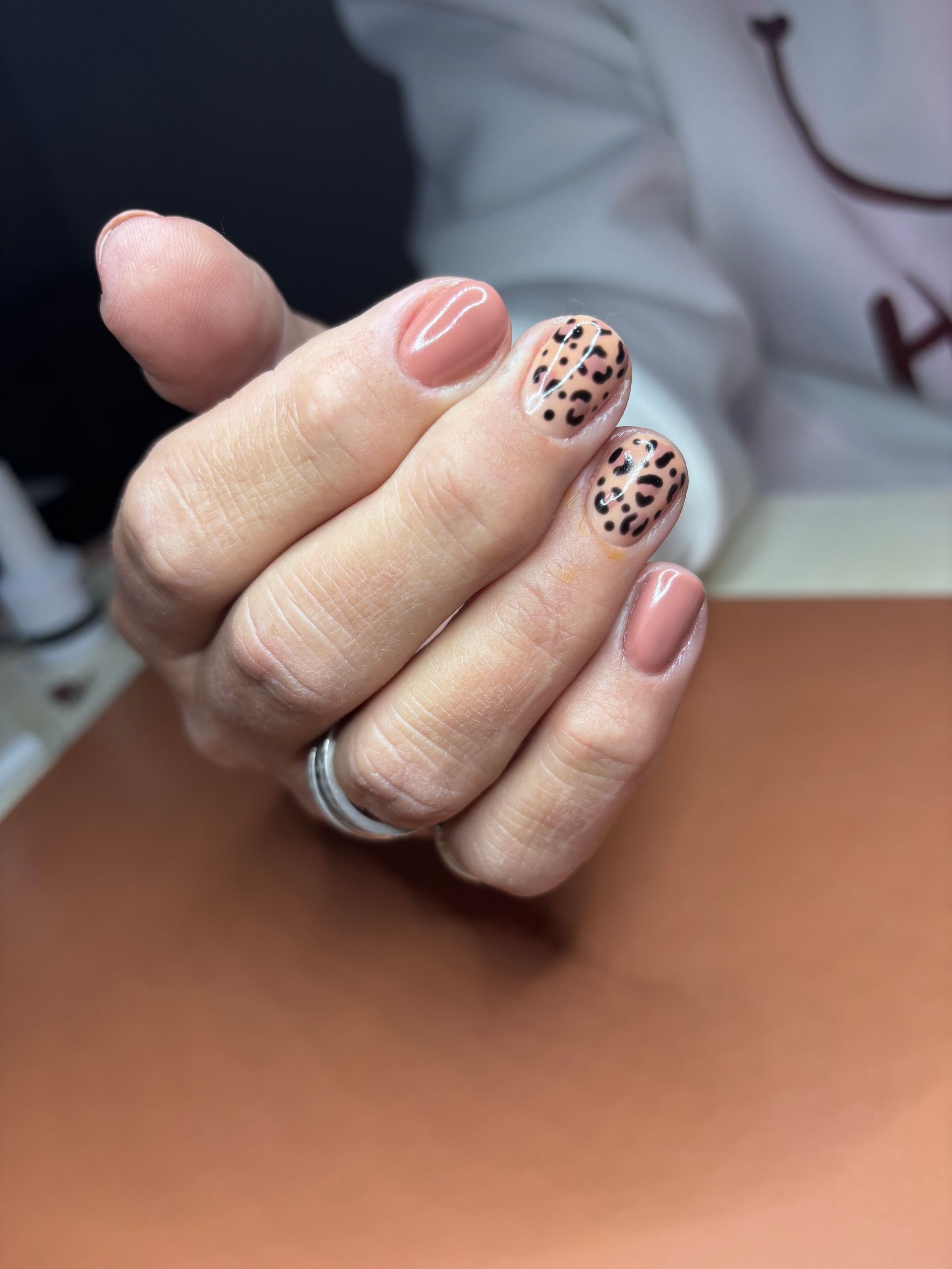 Hand met verzorgde nagels, sommige effen roze, andere met luipaardprint.