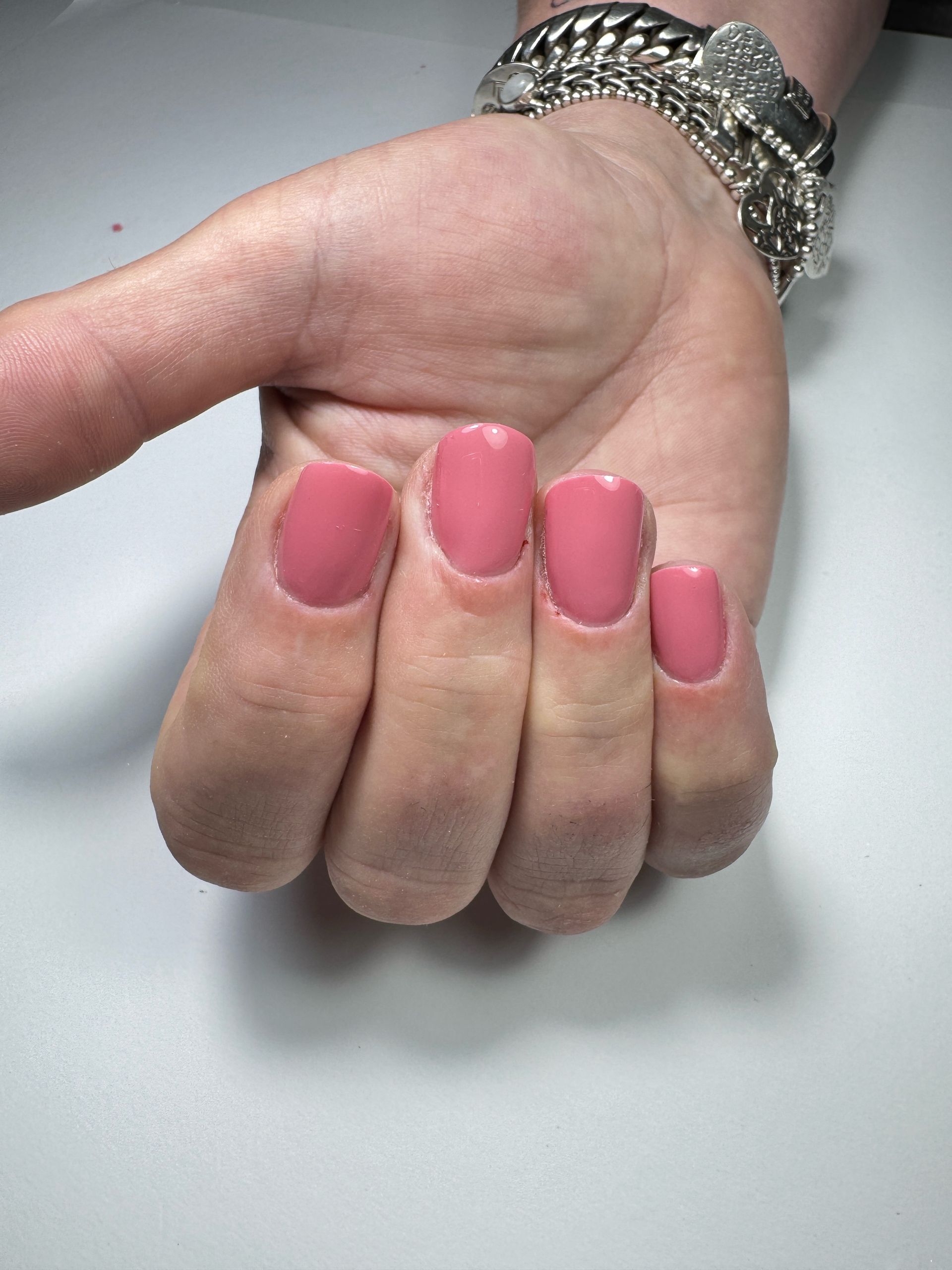Hand met roze vierkante nagels, voorzien van een zilveren armband, rustend op een witte ondergrond.