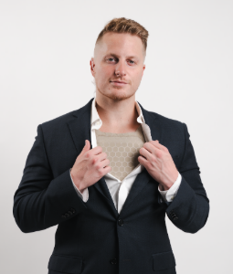 Man in suit pulls open shirt, revealing a protective chest plate.