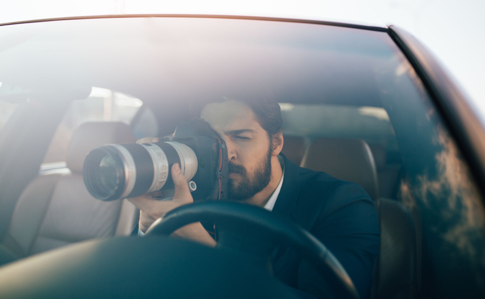 Person holding a long lens camera inside a car, capturing a scene through the windshield. Person holding a long lens camera inside a car, capturing a scene through the windshield.