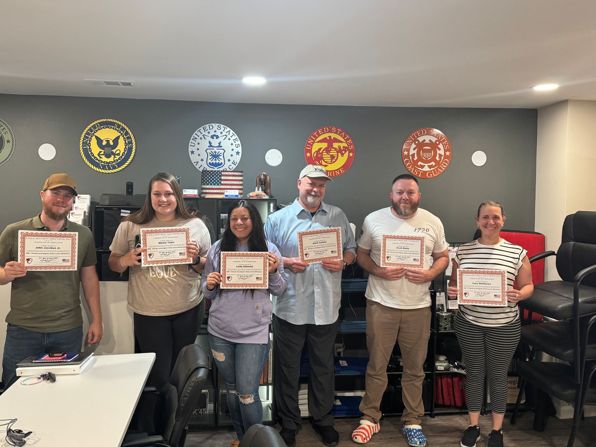 Group of people holding certificates, smiling, in front of military-themed wall decor.