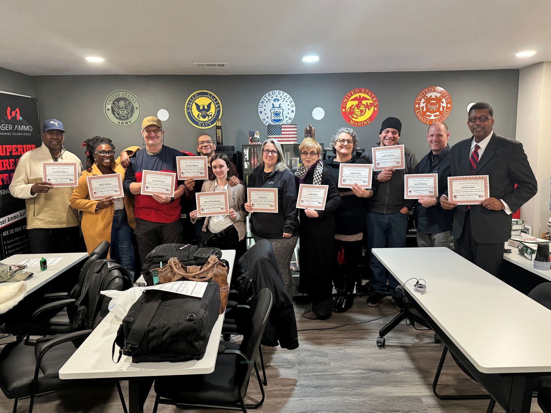 Group of people holding certificates, smiling in a room with logos on the wall.