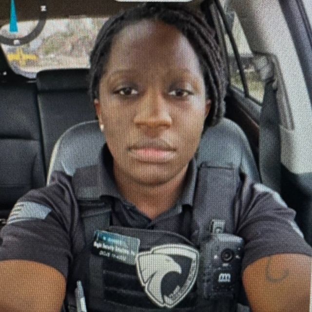 Woman in a security uniform, sitting in a vehicle, looking at the camera.