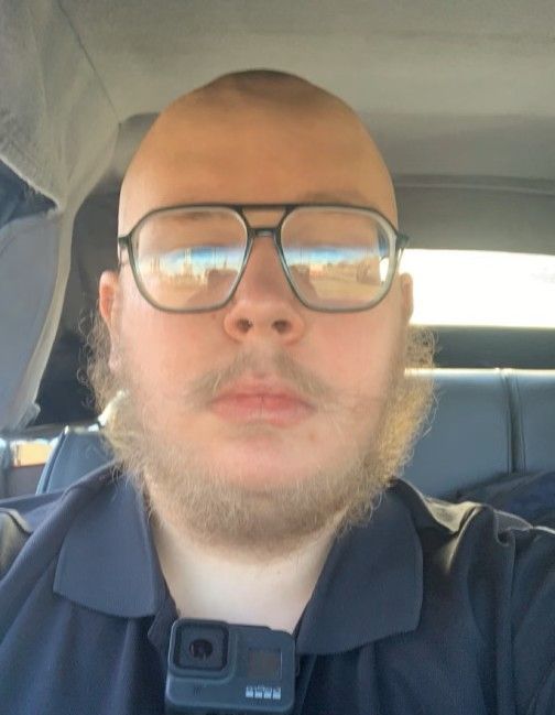 Person with glasses, shaved head, and beard; wearing a dark blue collared shirt; GoPro camera attached.