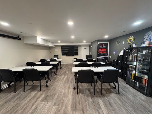 Classroom with gray flooring, tables, chairs, a large screen, and shelves.