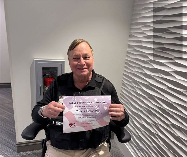 Man in wheelchair holds certificate, smiling. Next to textured wall.