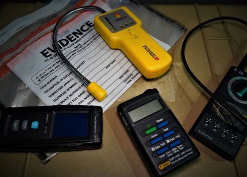 Assortment of scientific instruments, including a yellow detector, laid on a table next to an evidence bag.