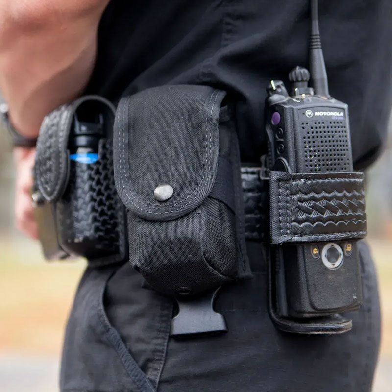 Police officer's duty belt holding pepper spray, a pouch, and a radio.