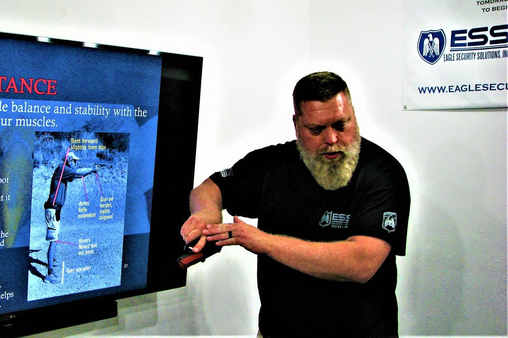 Man with a white beard gesturing towards a screen with text/image about balance.
