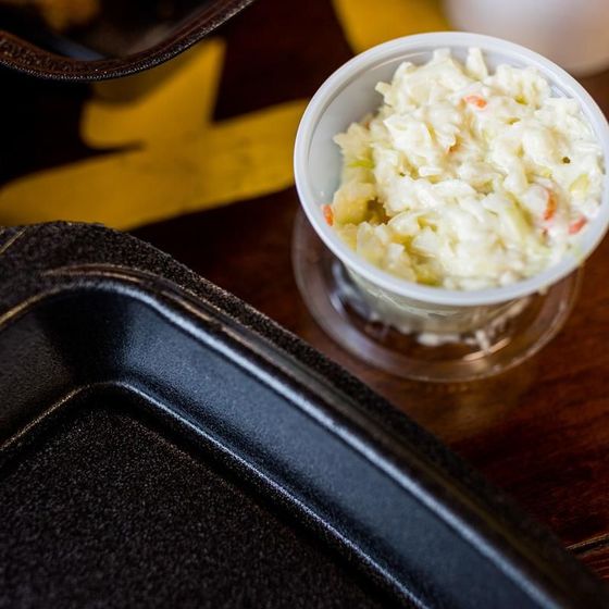 A bowl of coleslaw sits next to a black tray