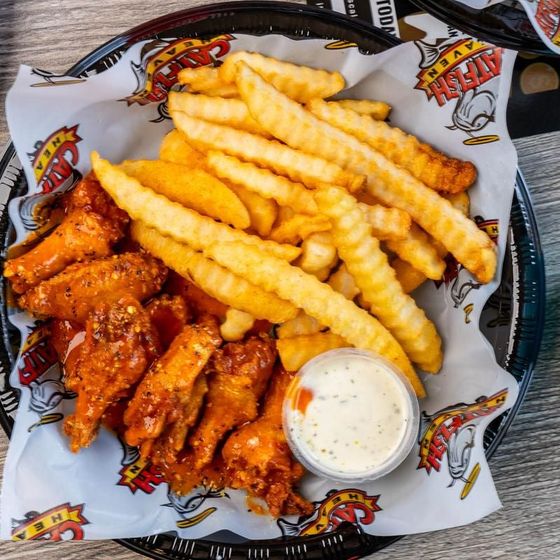 A basket of chicken wings and french fries with a dipping sauce