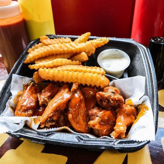 A styrofoam container filled with chicken wings and french fries