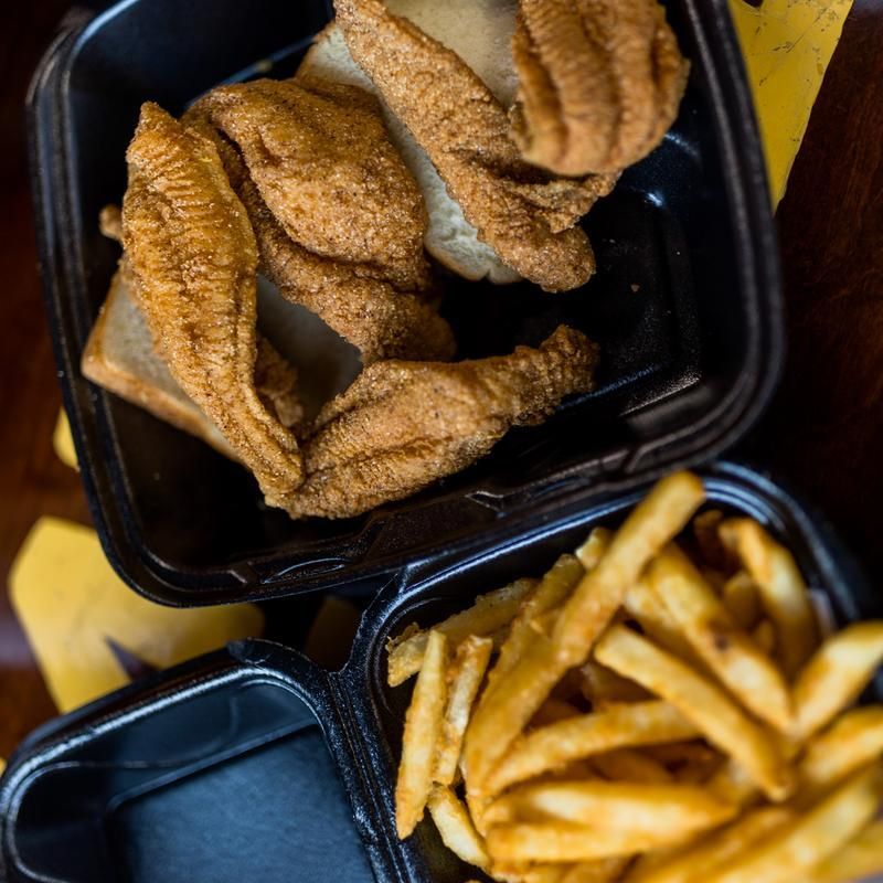 Fried fish and french fries in plastic containers on a table.