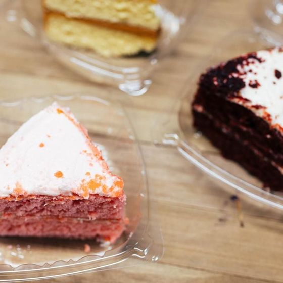 Two slices of cake are in plastic containers on a table