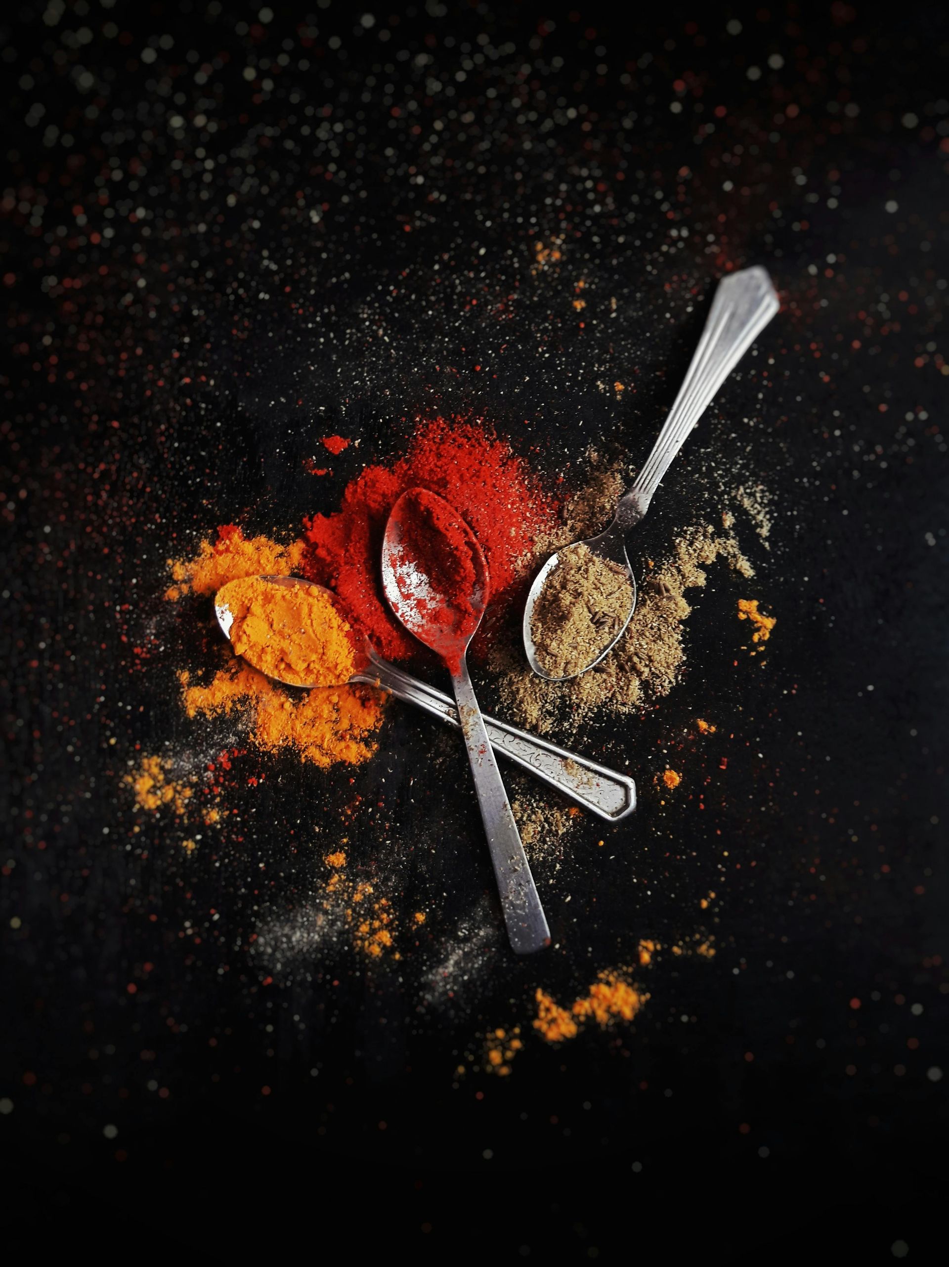 A bunch of spices and spoons on a black surface.