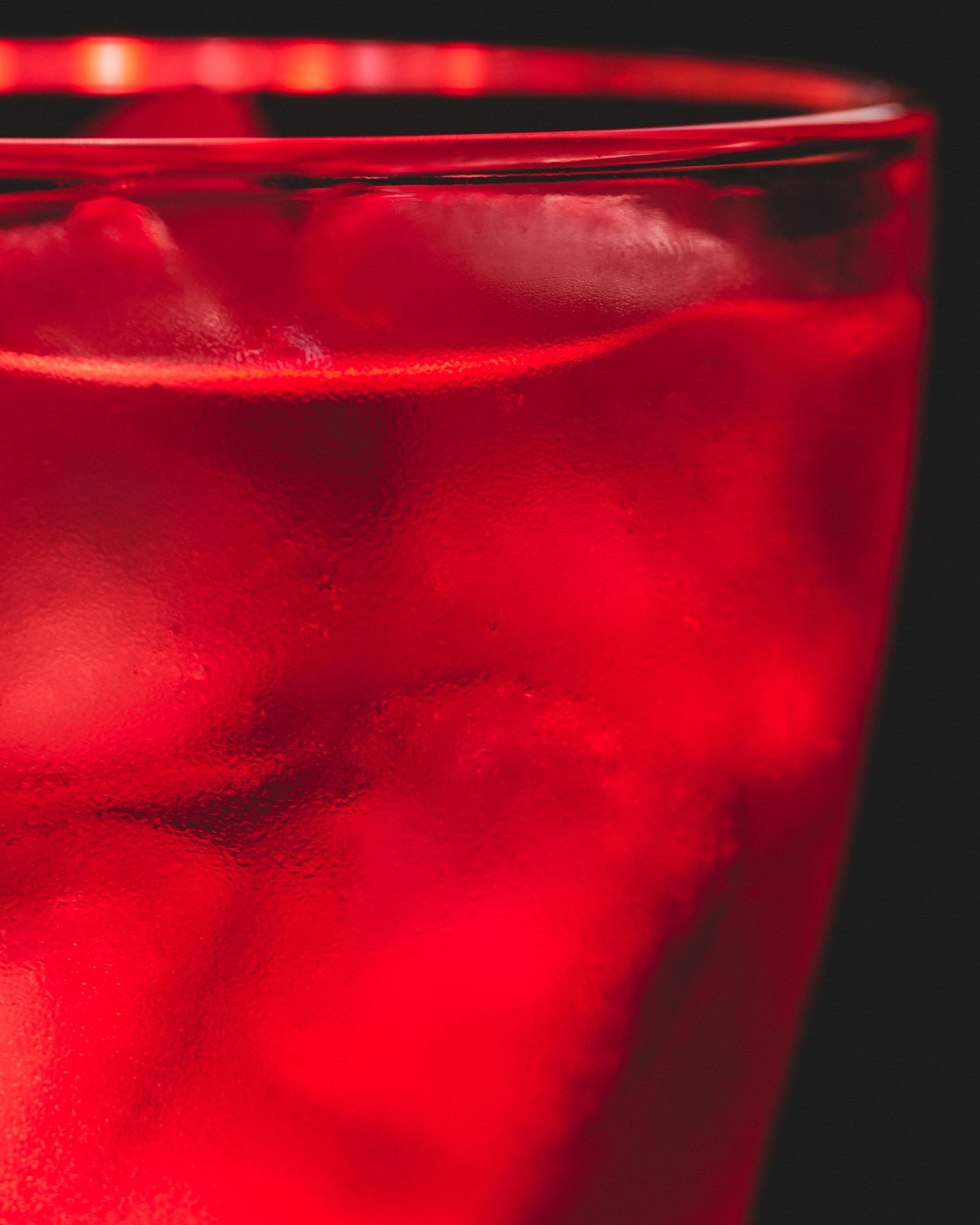 A close up of a red drink with ice in a glass.