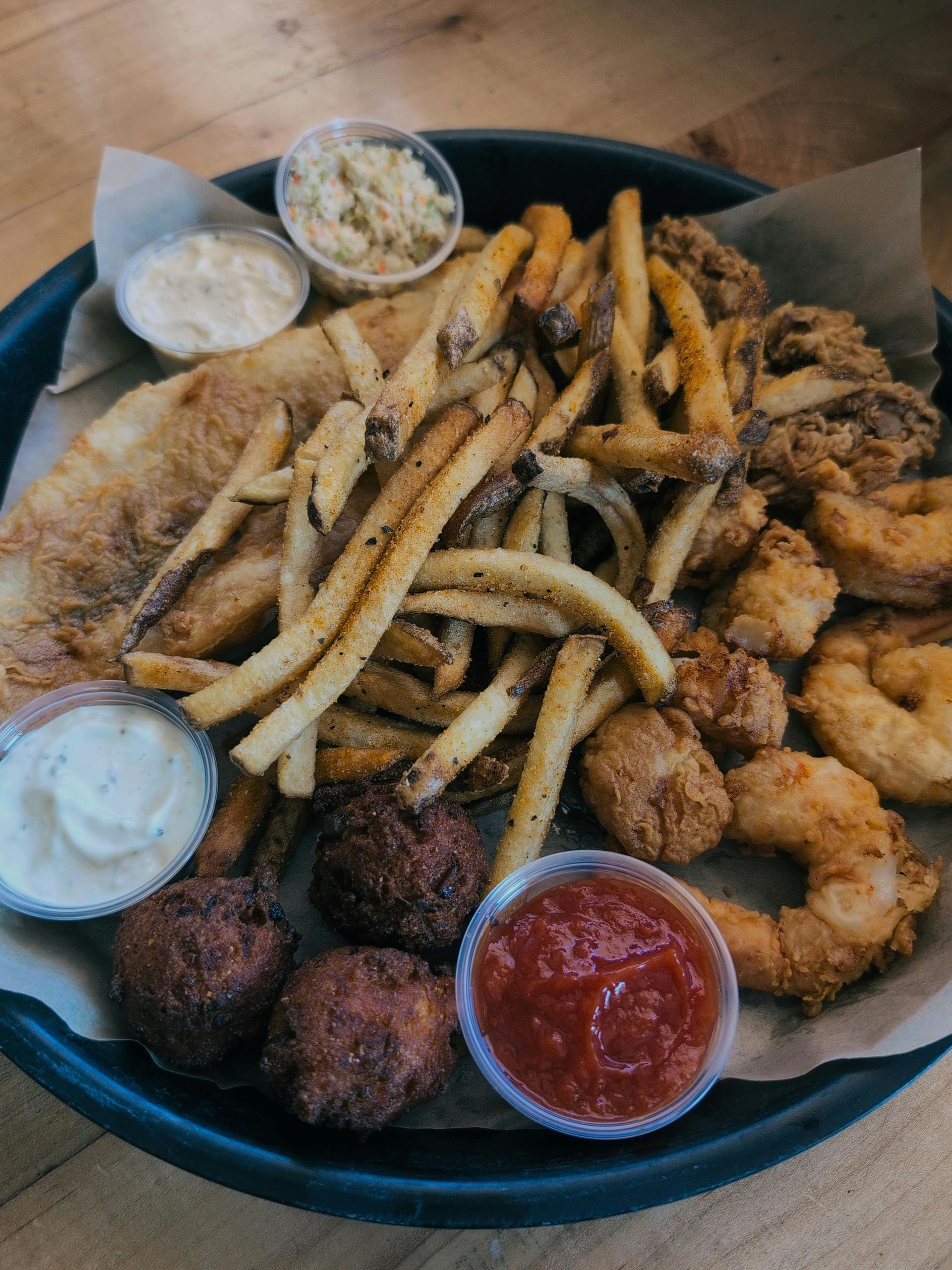 A tray of food with french fries , shrimp , onion rings and dips on a table.