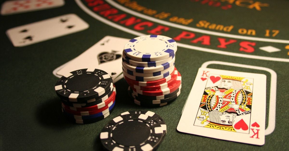 Stacks of casino chips sit beside playing cards on a green blackjack table under warm indoor lighting.