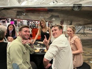 A group of people are sitting around a table with a plane in the background.