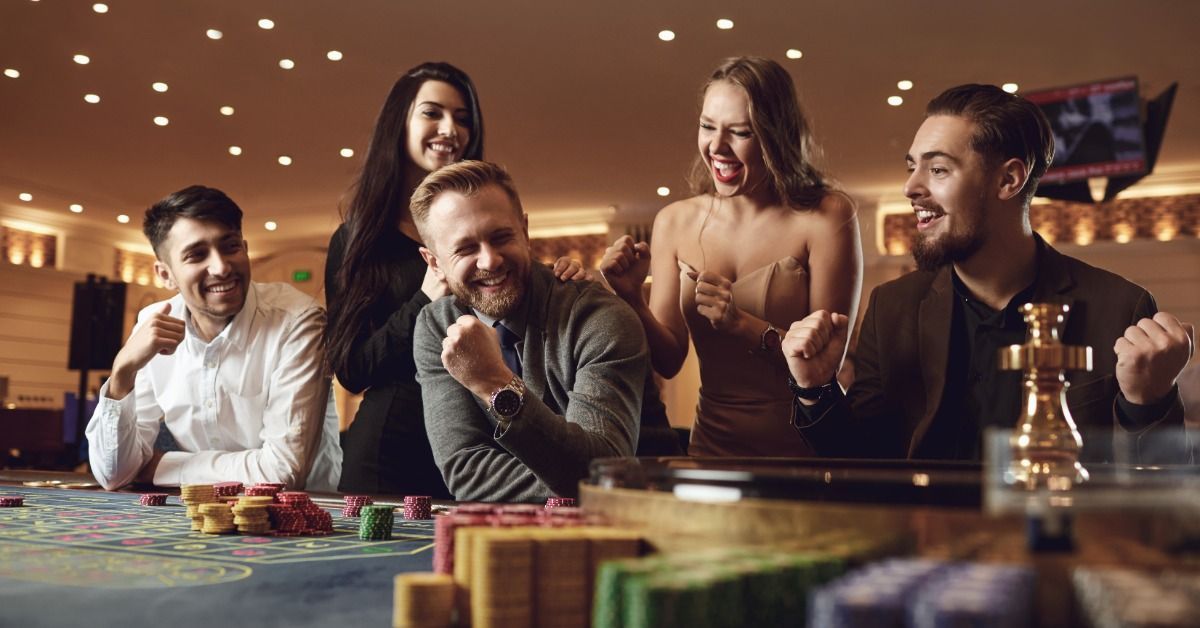 Five guests smiling and cheering around a casino gaming table with colorful chips.