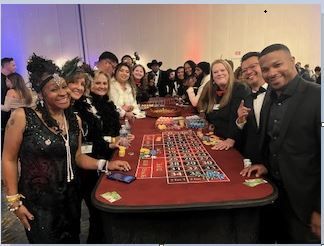 A group of people dressed in formal attire gathered around a red roulette table at an event.