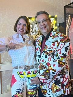 Two smiling people in colorful patterned outfits posing together indoors.