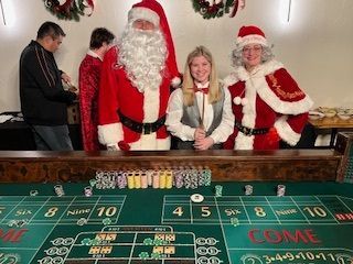 Santa and Mrs. Claus posing beside a craps table in a casino, with a smiling woman in the center