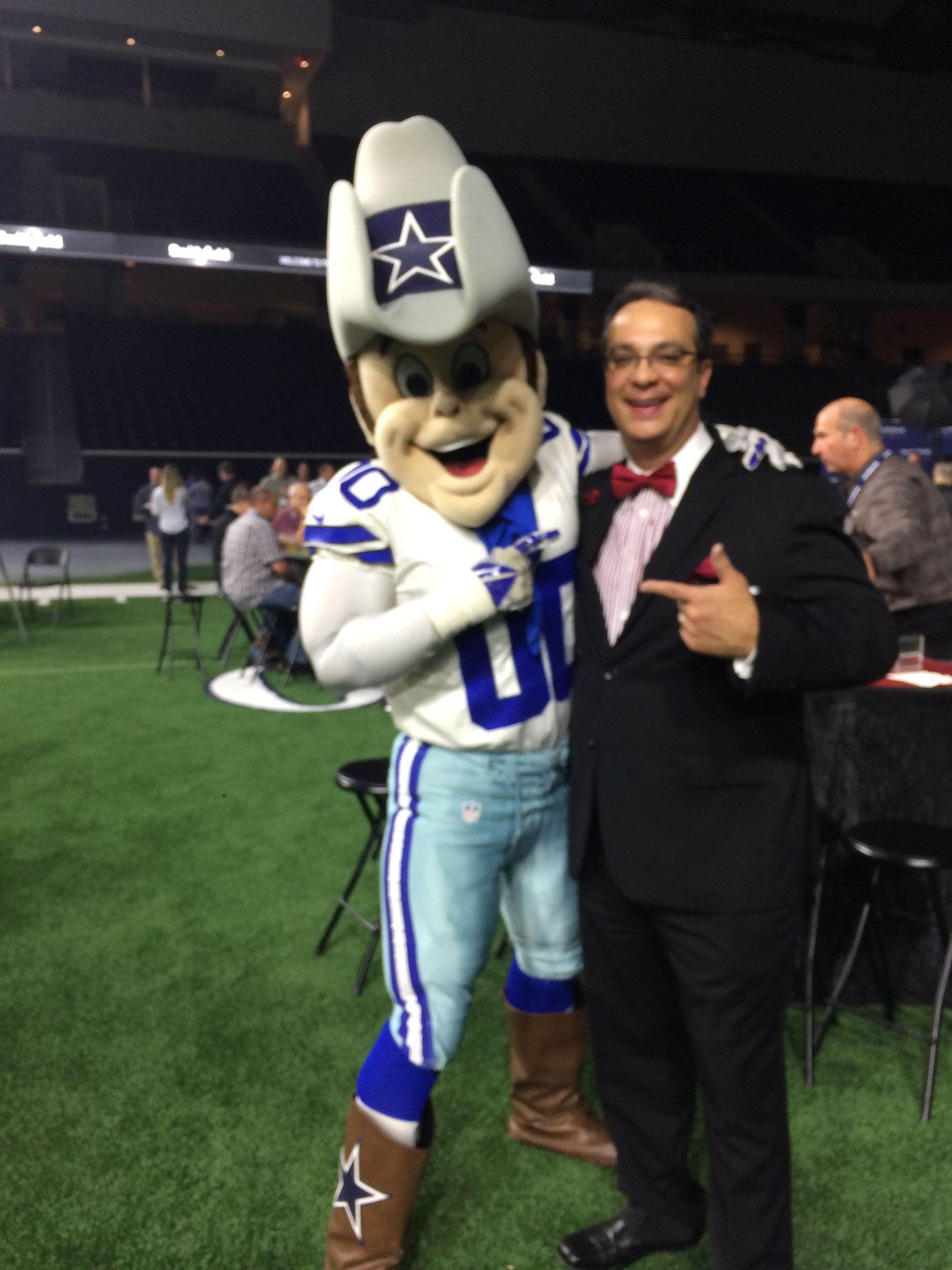 Dallas Cowboys mascot poses with a man in a tuxedo on a football field.