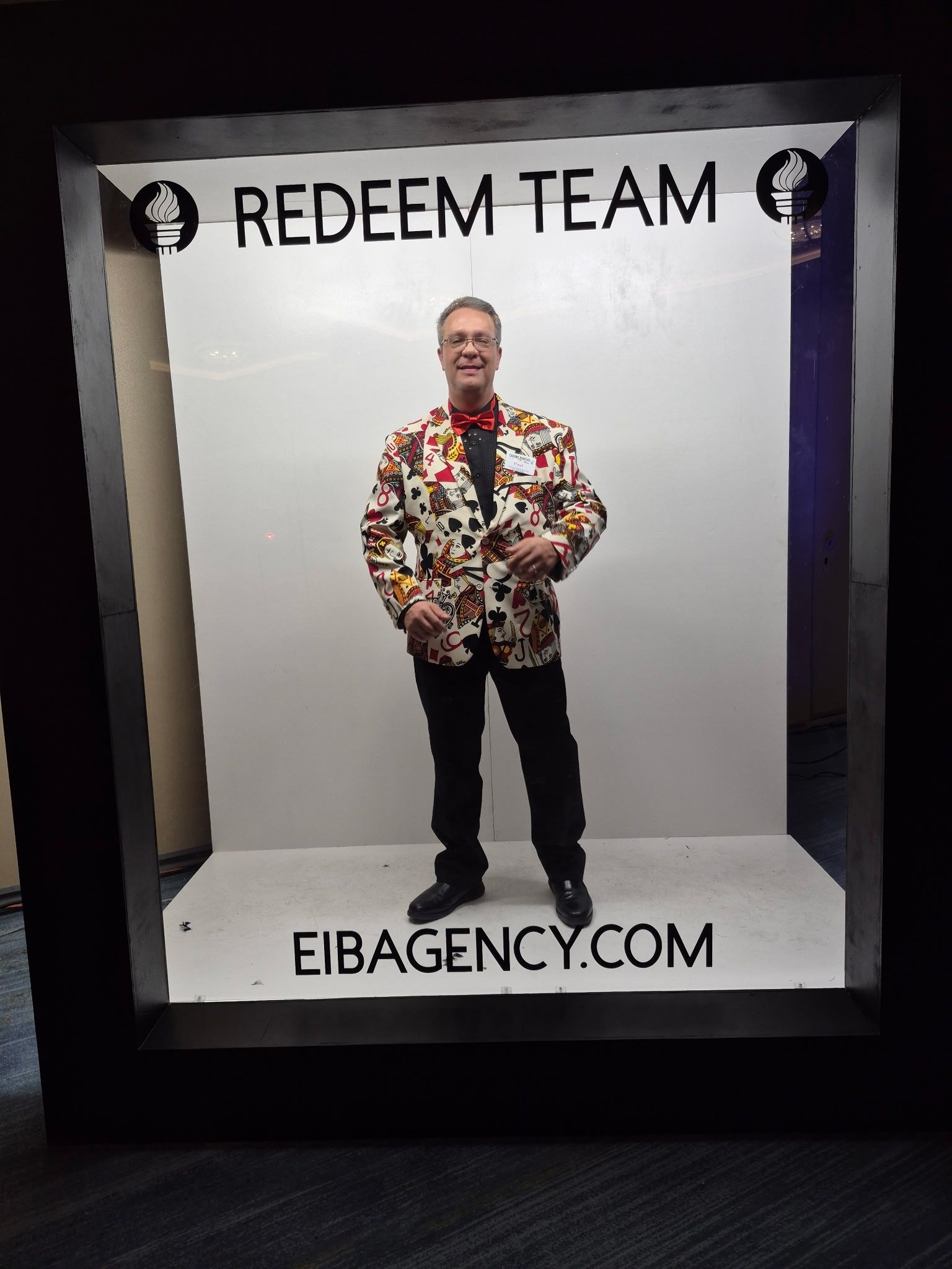 A person wearing a patterned blazer and bowtie stands inside a frame labeled 