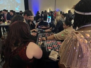 People gather around a roulette table at a formal event, placing bets and watching the game.