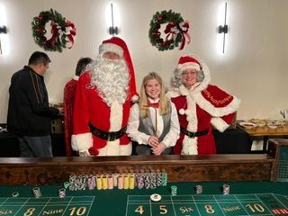 Santa and Mrs. Claus posing with a smiling woman at a casino table during a holiday event