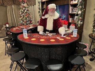 Santa seated at a casino-style Christmas table with chips, surrounded by stools and holiday decor