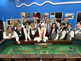 Casino group posing behind a roulette table in a blue room with framed pictures on the wall